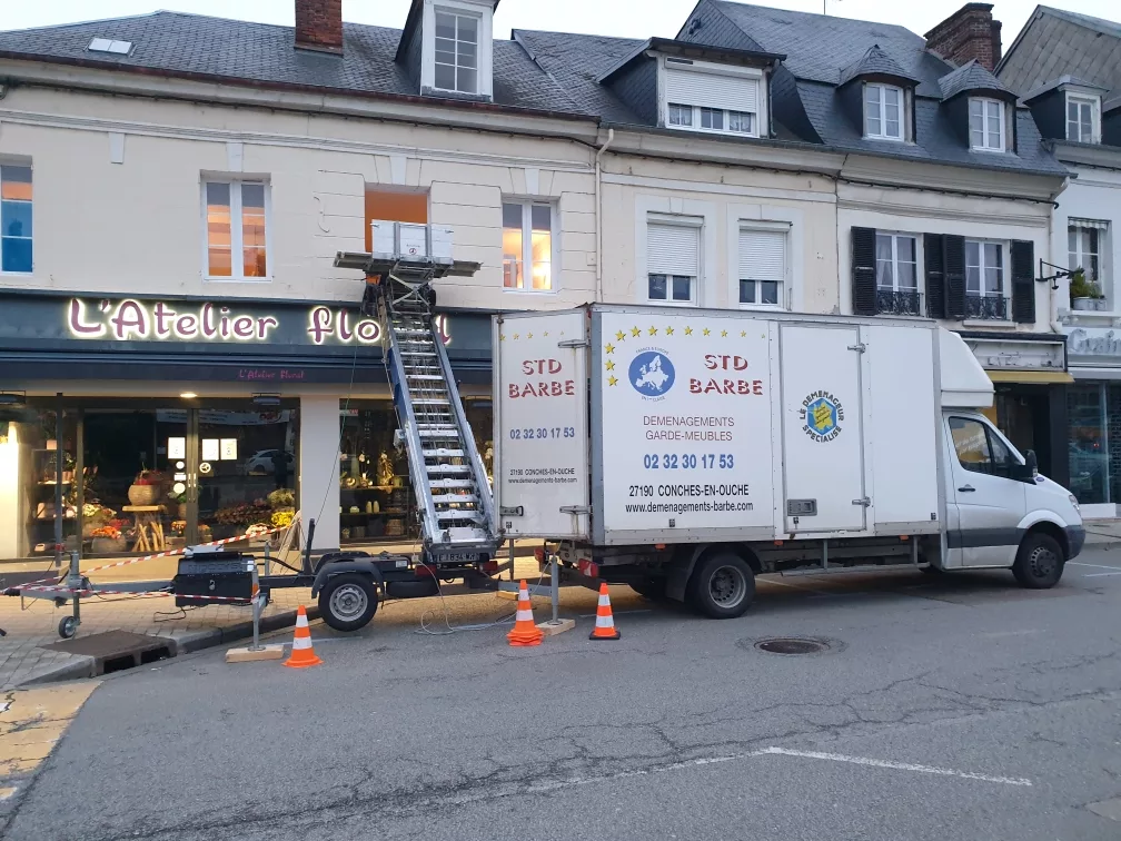 Un camion de déménagement STD BARBE est garé devant un bâtiment.