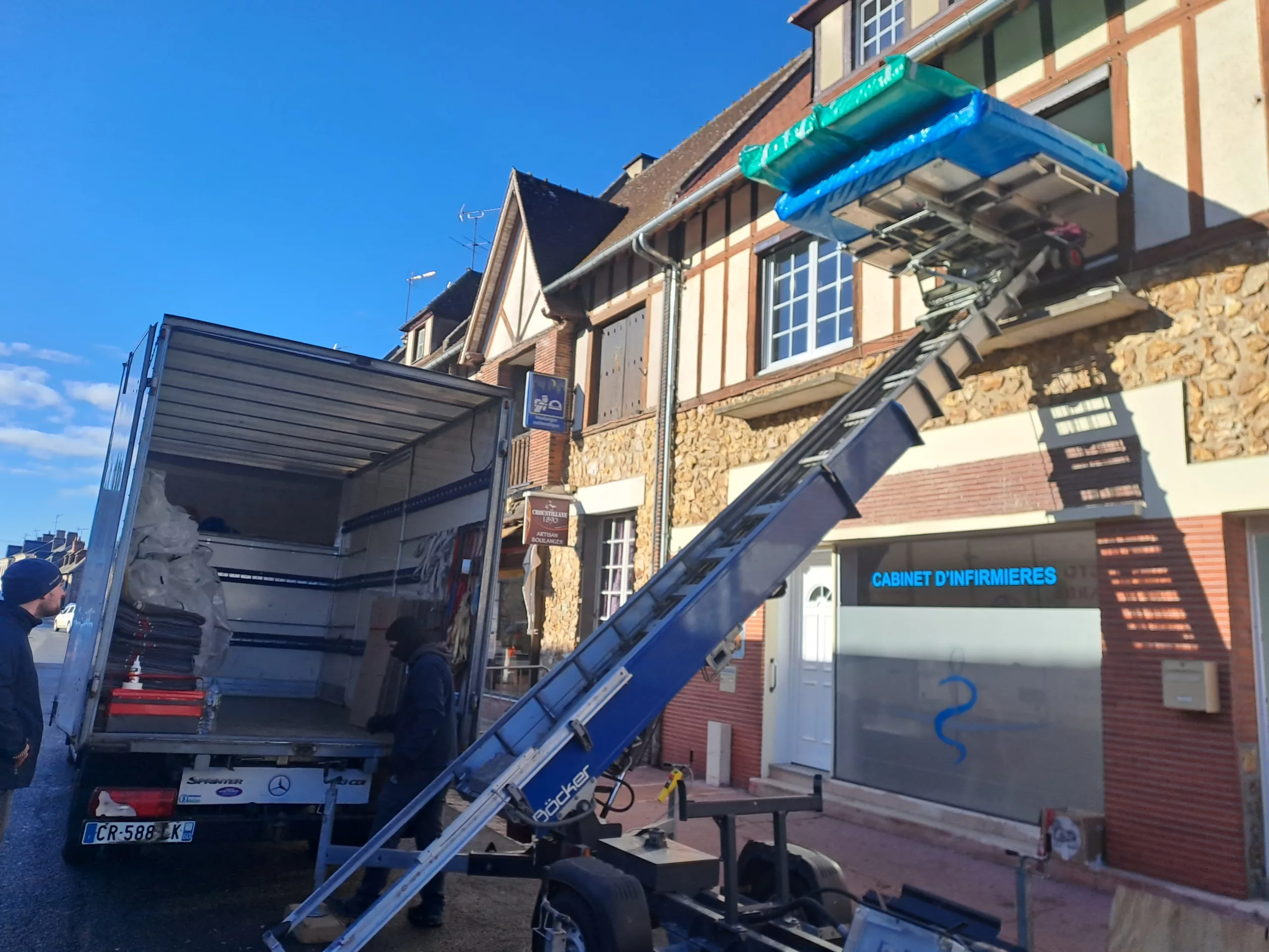 Un homme charge sur une échelle bleue des cartons emballés dans un camion.