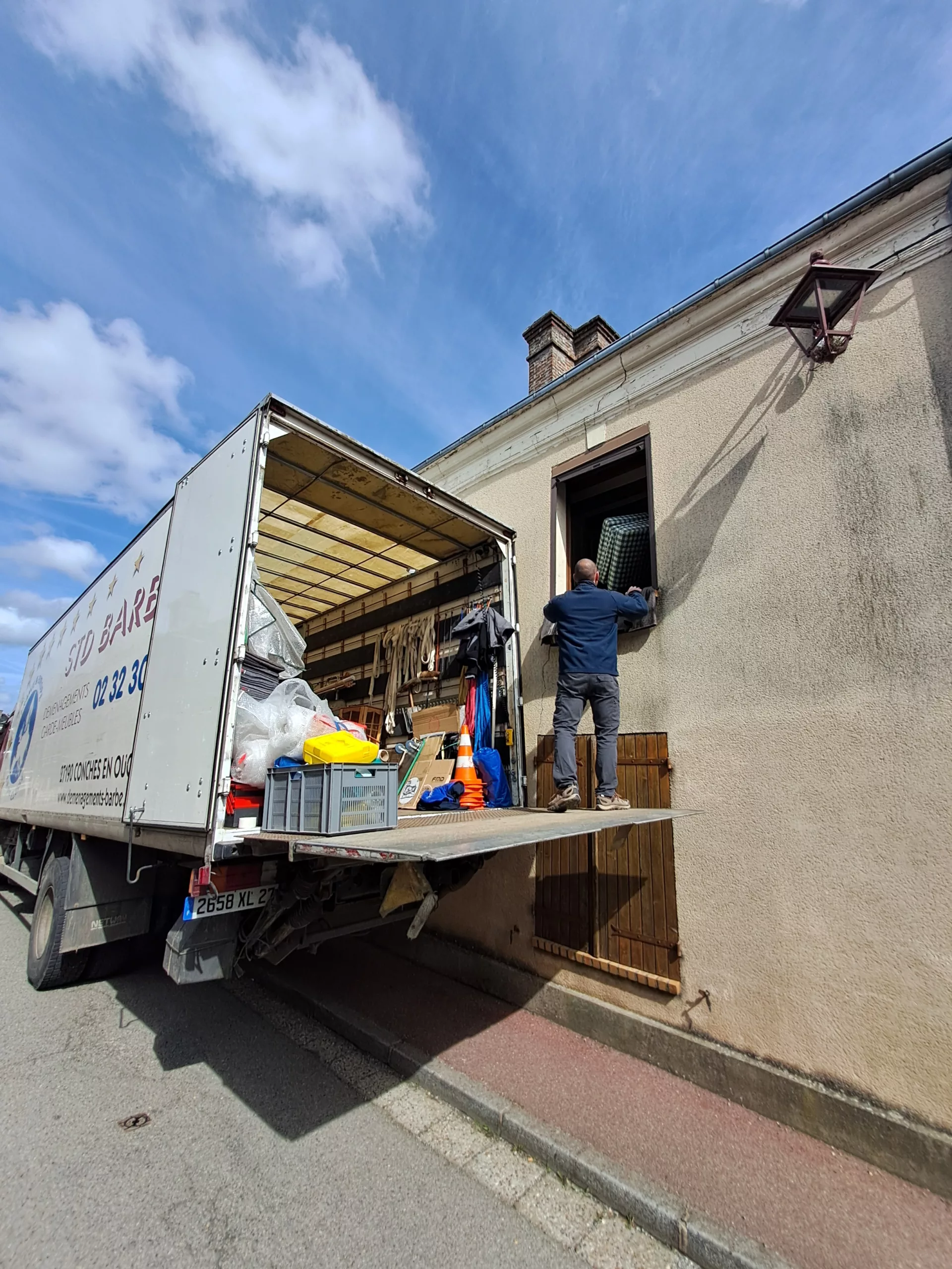 Un homme sur le dos d'un camion de déménagement STD BARBE, en plein déménagement sur le bord de la route.